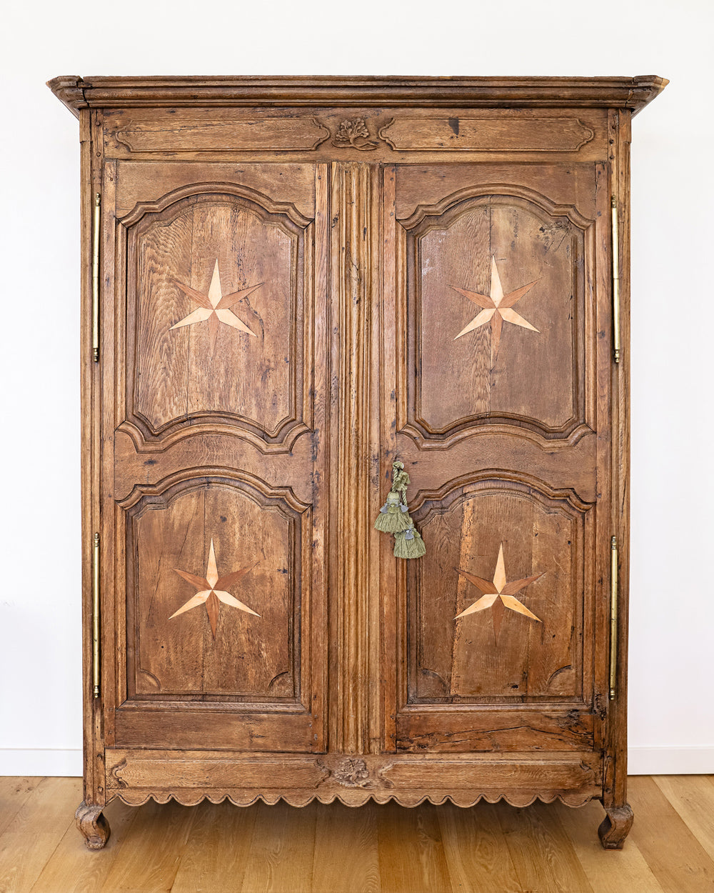 Antique French Louis XV style armoire with star shaped inlays on the doors, made of wood with a visible rustic finish, placed on a wooden floor.