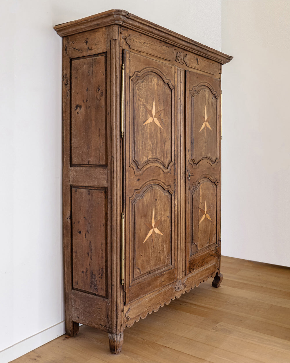 Sideview of an antique French Louis XV style armoire with star shaped inlays on the doors, made of wood with a visible rustic finish, placed on a wooden floor and available at Wildschut Antiques