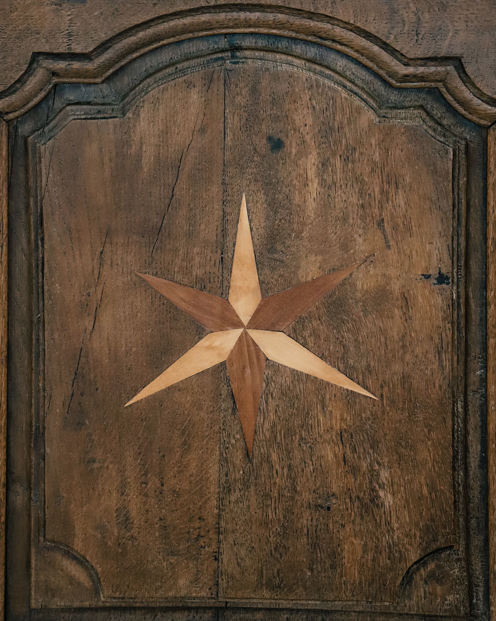 Close-up of a door panel of an antique French Louis XV style armoire with star shaped inlays on the doors, made of wood with a visible rustic finish