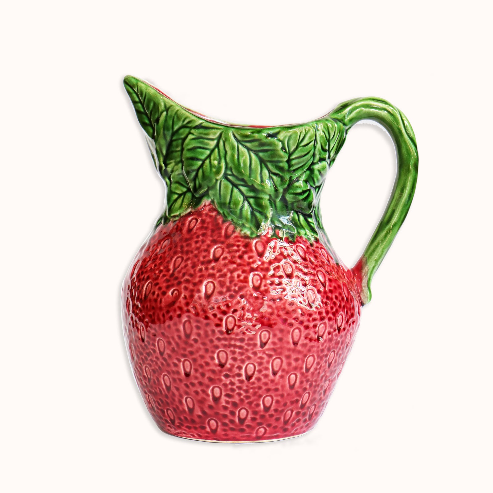 A vintage ceramic pitcher or jug shaped like a strawberry with a green leaf pattern on the handle, available at Wildschut Antiques