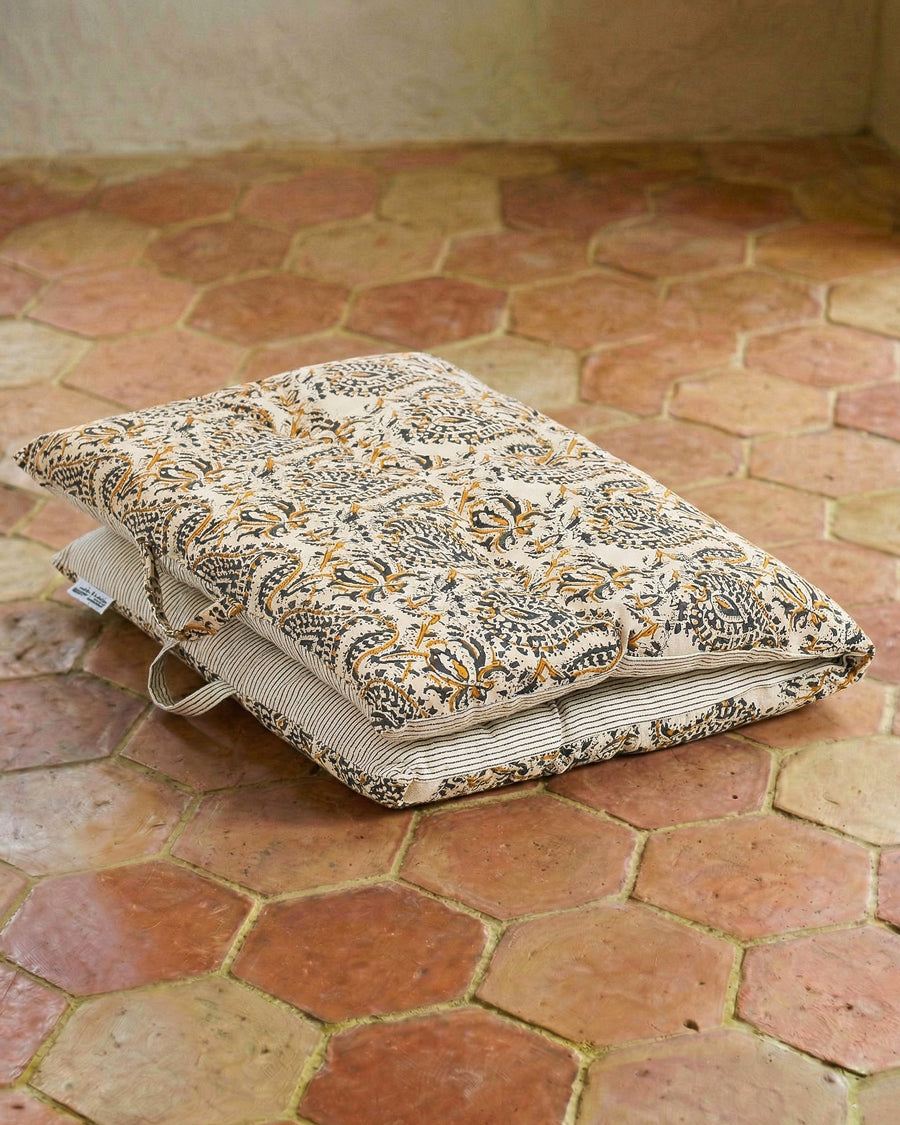 Decorative pillow with a floral pattern on a terracotta floor. Mattress pillow available via Wildschut Antiques.