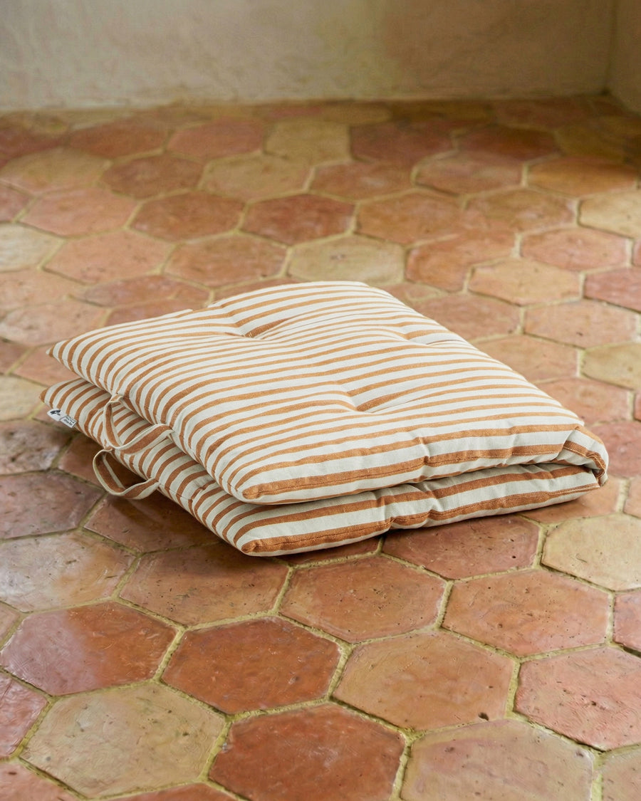 Folded striped cushion on a terracotta tiled floor. Mattress pillow available via Wildschut Antiques.