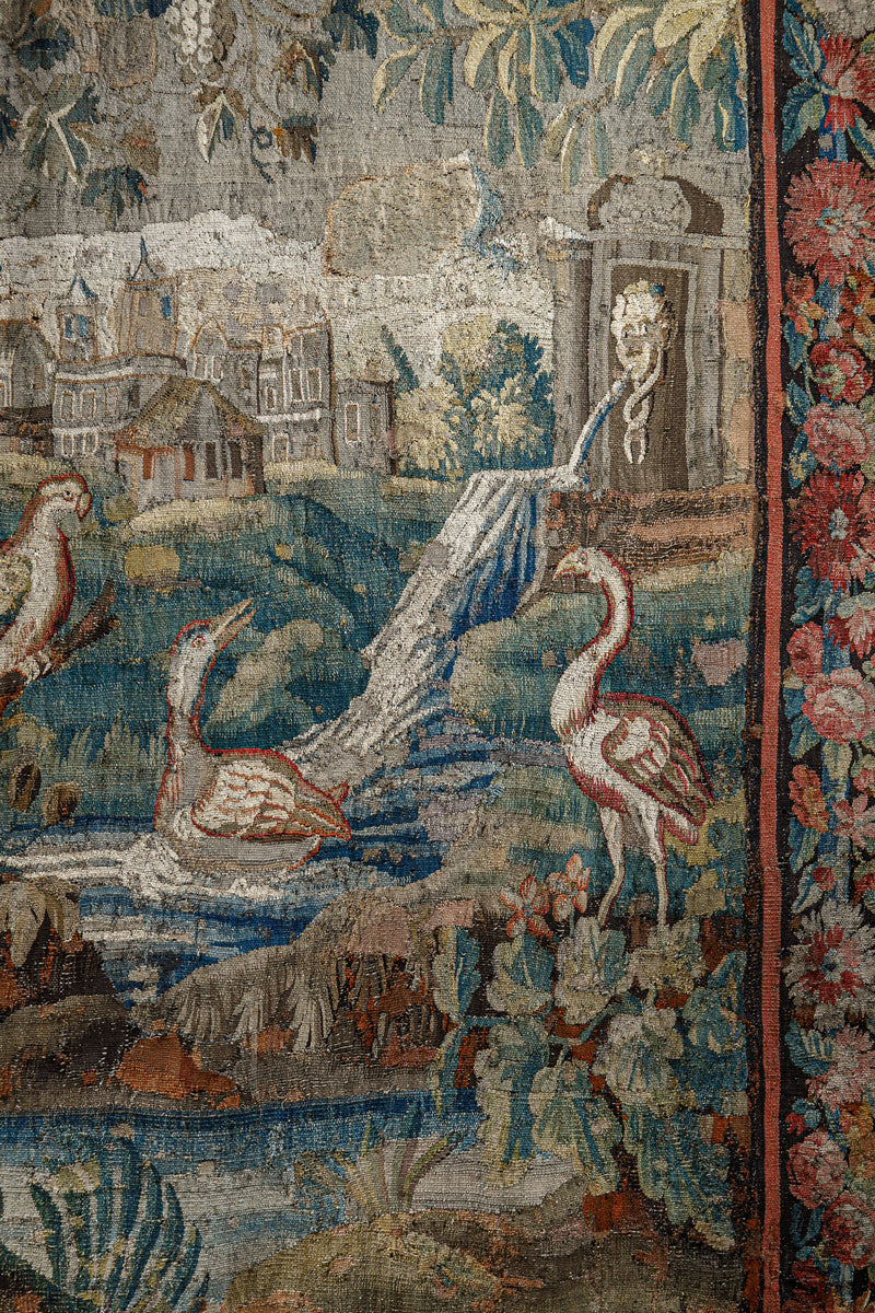 Close-up of a decorative 18th-century Verdure tapestry with birds, flowers, leaves, and a landscape.