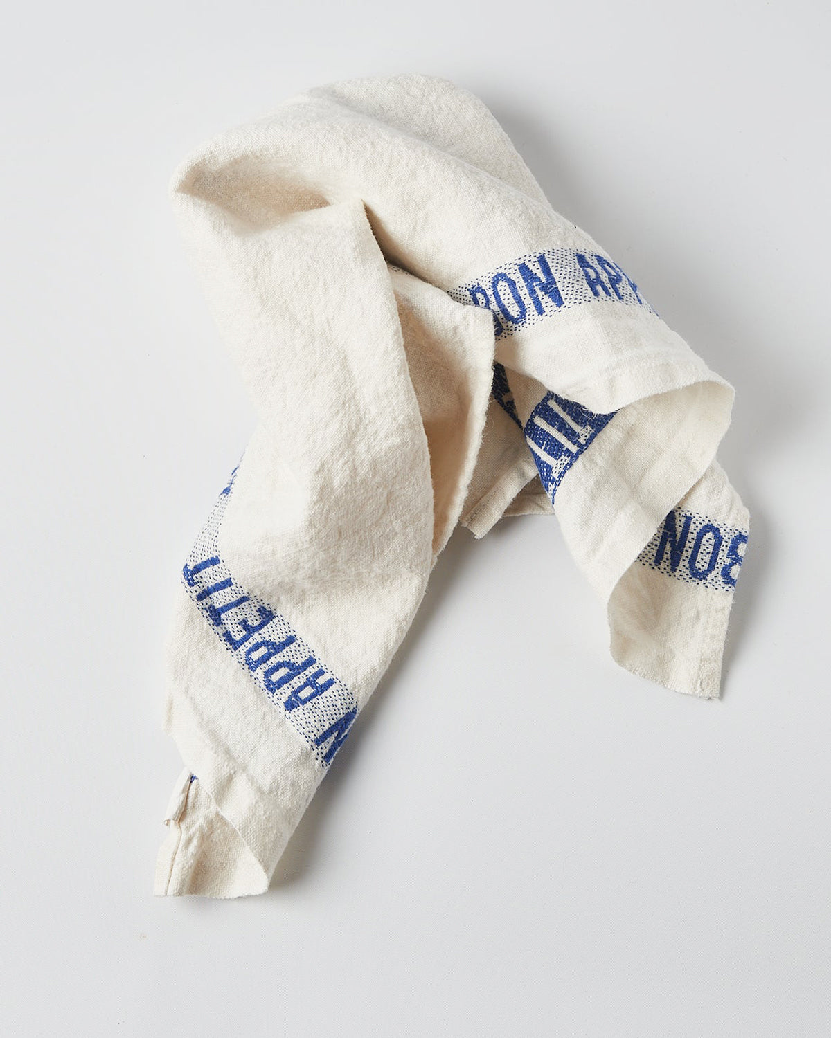 Folded white linen dish towel with 'BON APPÉTIT' embroidered in blue along the edges, by Charvet Editions, available at Wildschut Antiques