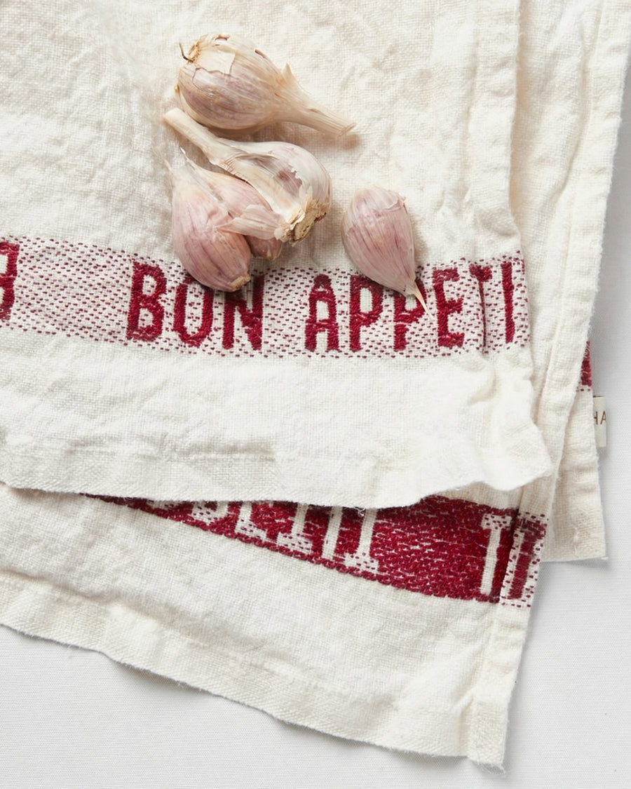 Close-up of a linen towel with 'Bon Appetit' text in red and garlic bulbs on a white background, by Charvet Editions available via Wildschut Antiques.