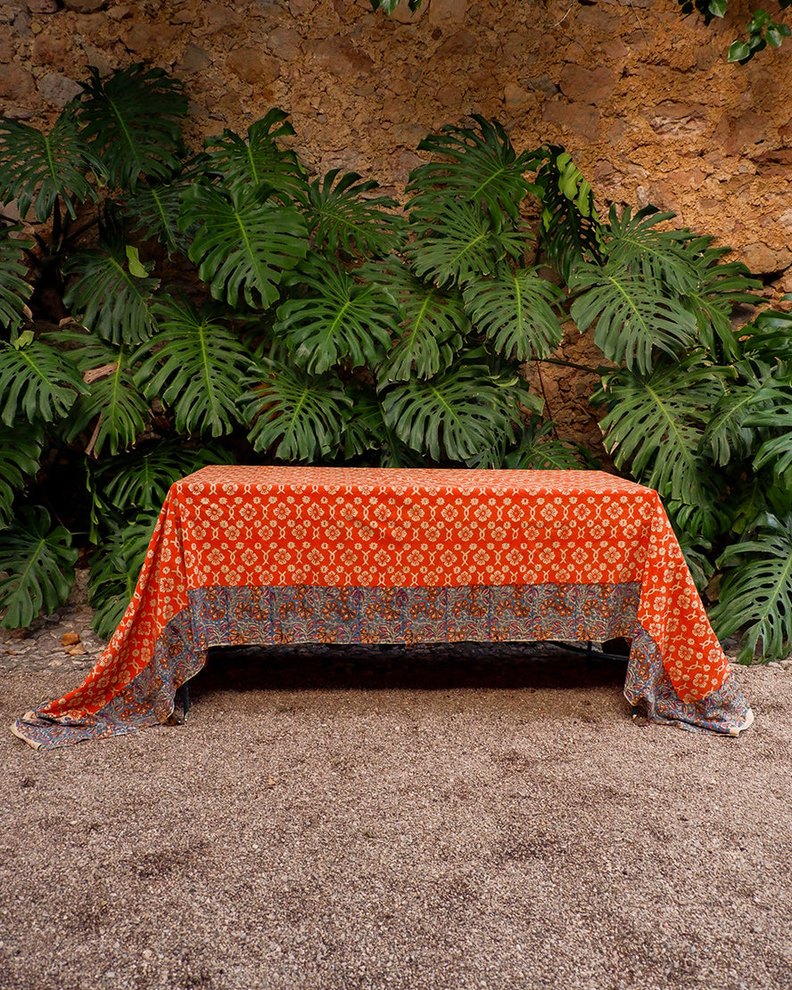 Orange patterned tablecloth on a wooden table with green plants in the background