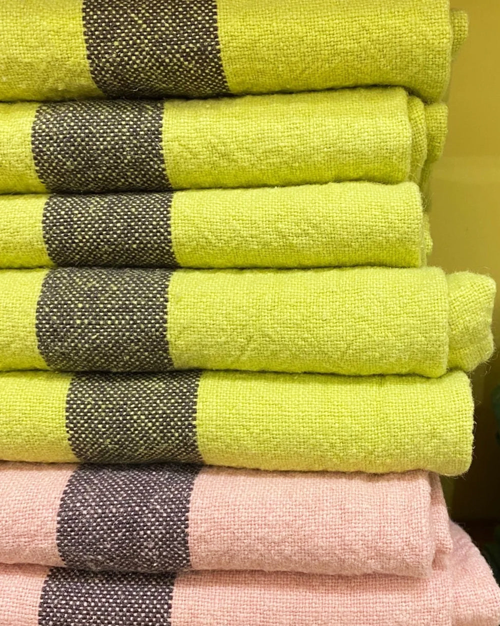 A pile of neatly folded linen dish towels in yellow and soft pink by Charvet Editions available at Wildschut Antiques