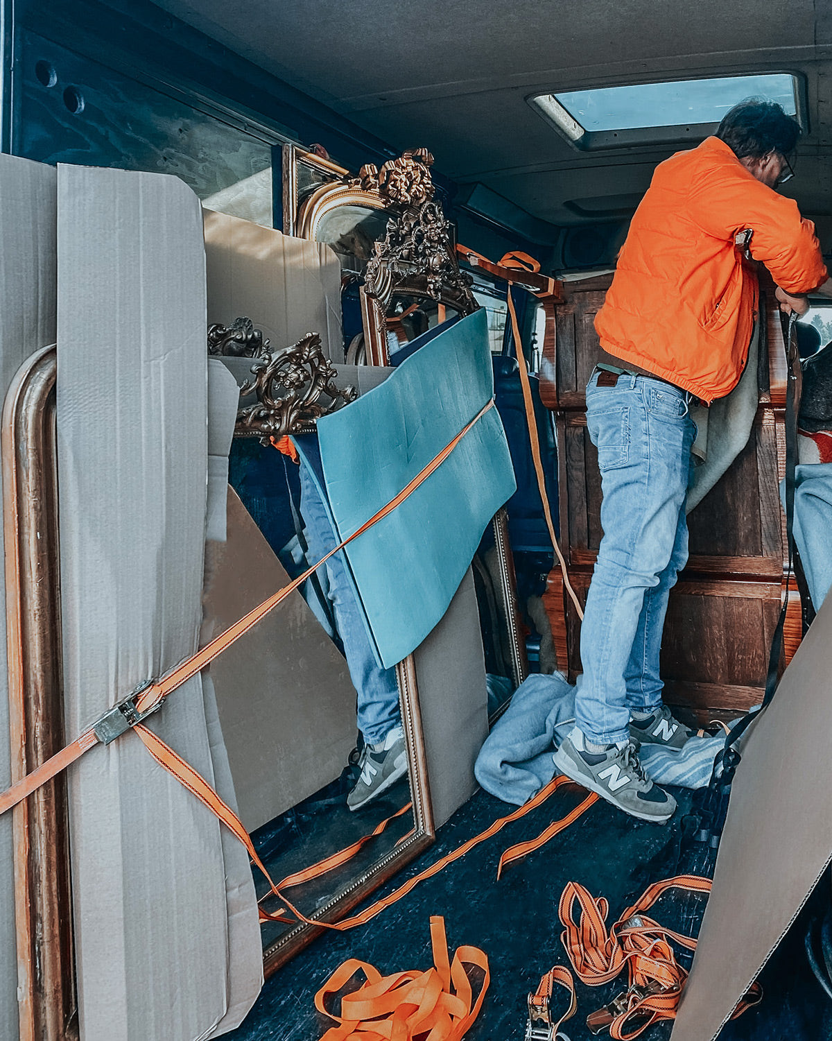 Michiel Wildschut in an orange puffer jacket, securing antique mirrors in the back of his van.