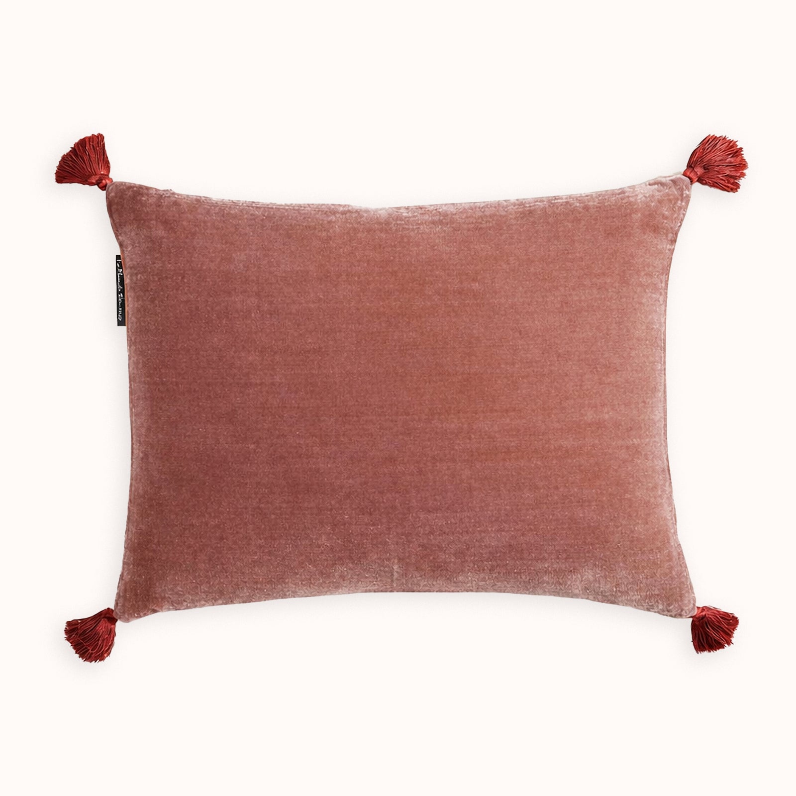 Dark peach pink silk velvet velour cushion with contrasting pom-pom tassel details on a white background. Designed by Monde Sauvage Paris, available at Wildschut Antiques.