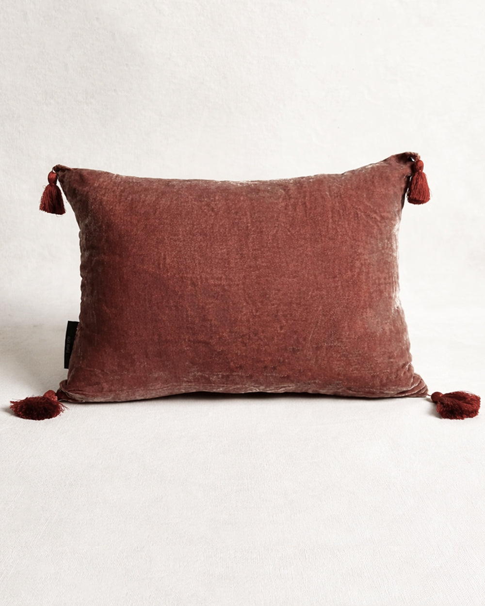 Dark peach pink silk velvet velour cushion with contrasting pom-pom tassel details on a light grey background. Designed by Monde Sauvage Paris, available at Wildschut Antiques.