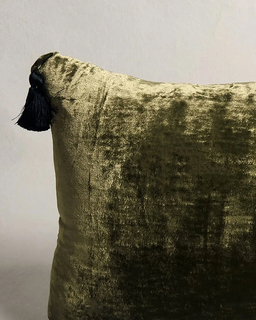Close-up of a dark olive green silk velvet velour pillow with contrasting pom-pom tassel details on a light grey background. Designed by Monde Sauvage Paris, available at Wildschut Antiques.