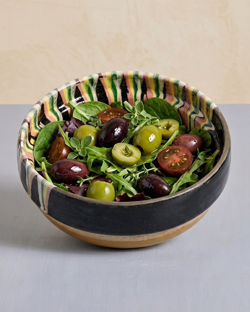 Decorative bowl with a salad of greens, olives, and tomatoes on a neutral background