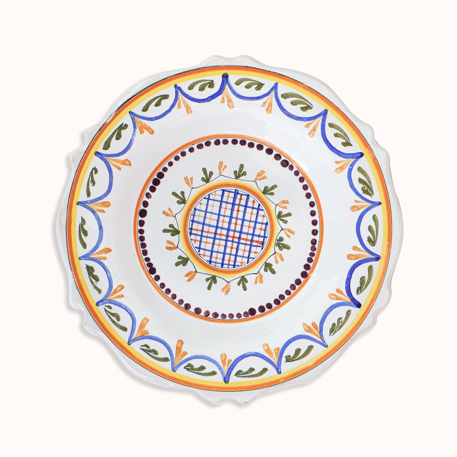 A small, vintage, hand-painted majolica ceramic plate with a geometric pattern, featuring swirls and foliate motifs in a combination of blue, green, and orange colors on a white background