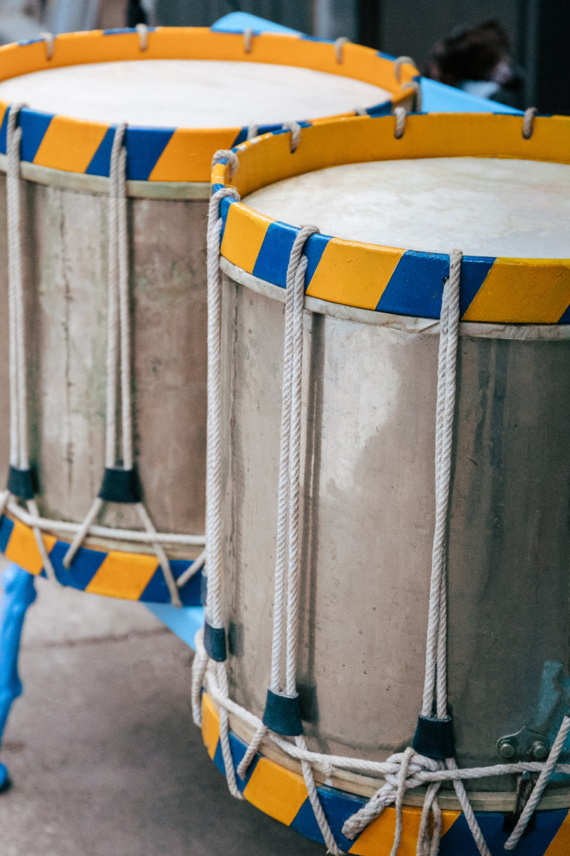 Close-up of two vintage drums with blue and yellow paint, and silver drum heads, bound by ropes