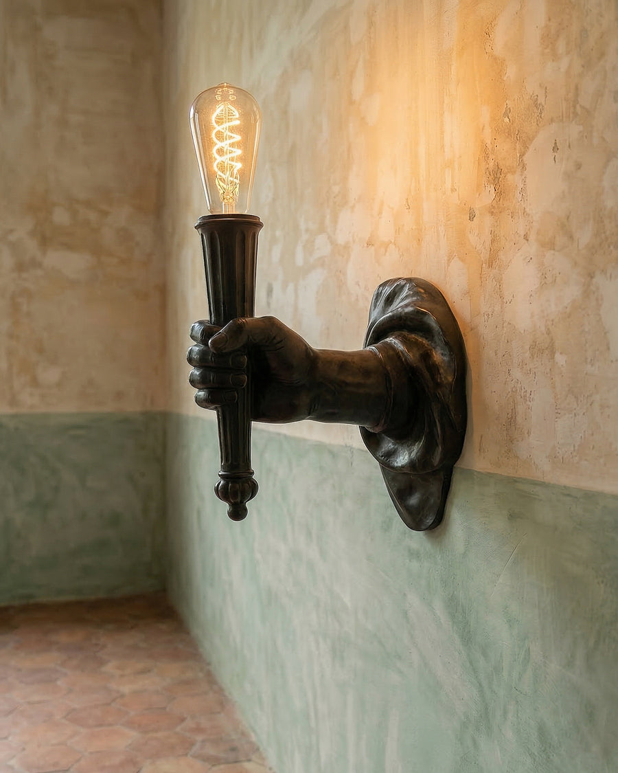 Decorative wall light fixture in the form of a stretched hand and arm with a vintage-style bulb on a textured wall, available via Wildschut Antiques.