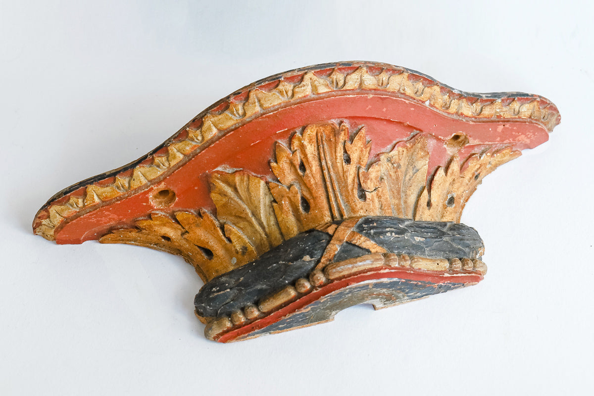 A small antique French carved and gilded wall bracket, with original paint and a richly aged patina in red, blue, and gold tones.