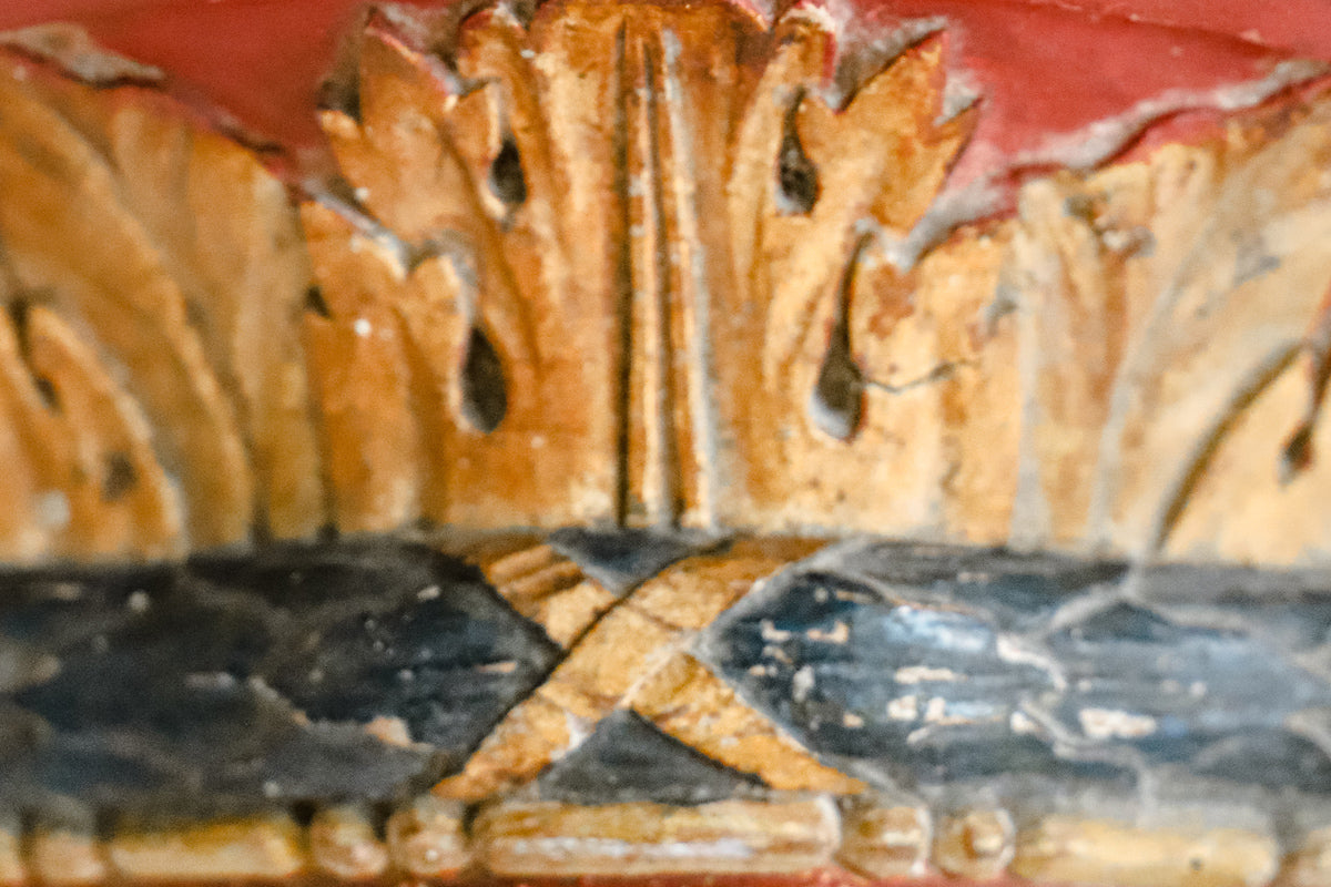 Close-up of a small antique French carved and gilded wall bracket, with original paint and a richly aged patina in red, blue, and gold tones.