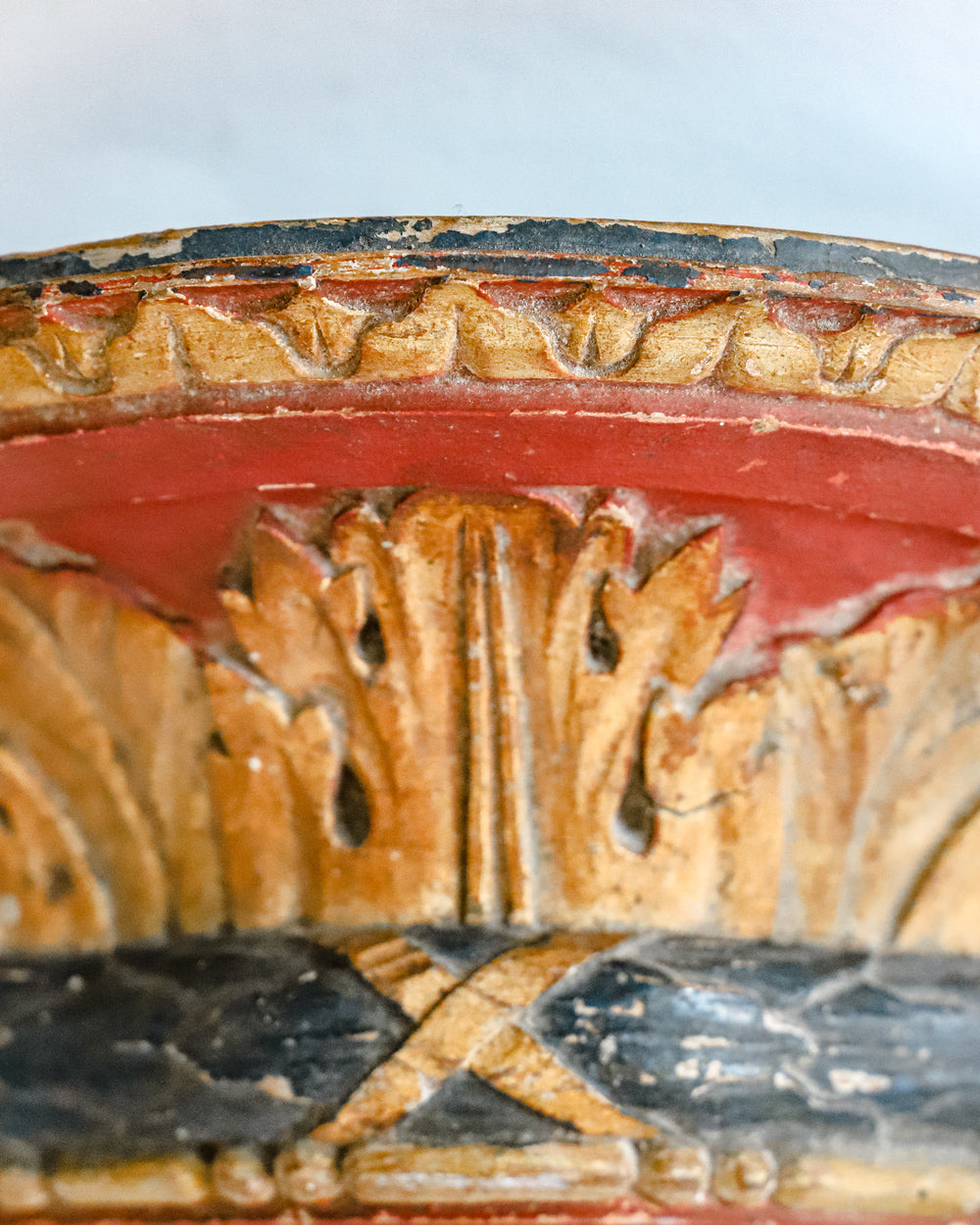 Detail of a small antique French carved and gilded wall bracket, with original paint and a richly aged patina in red, blue, and gold tones.