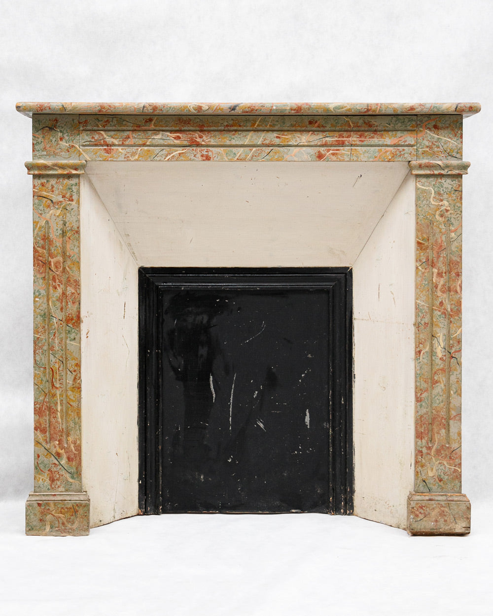 19th-century French antique wooden fireplace with faux marble painting in a colorful pattern on a white background, available at Wildschut Antiques