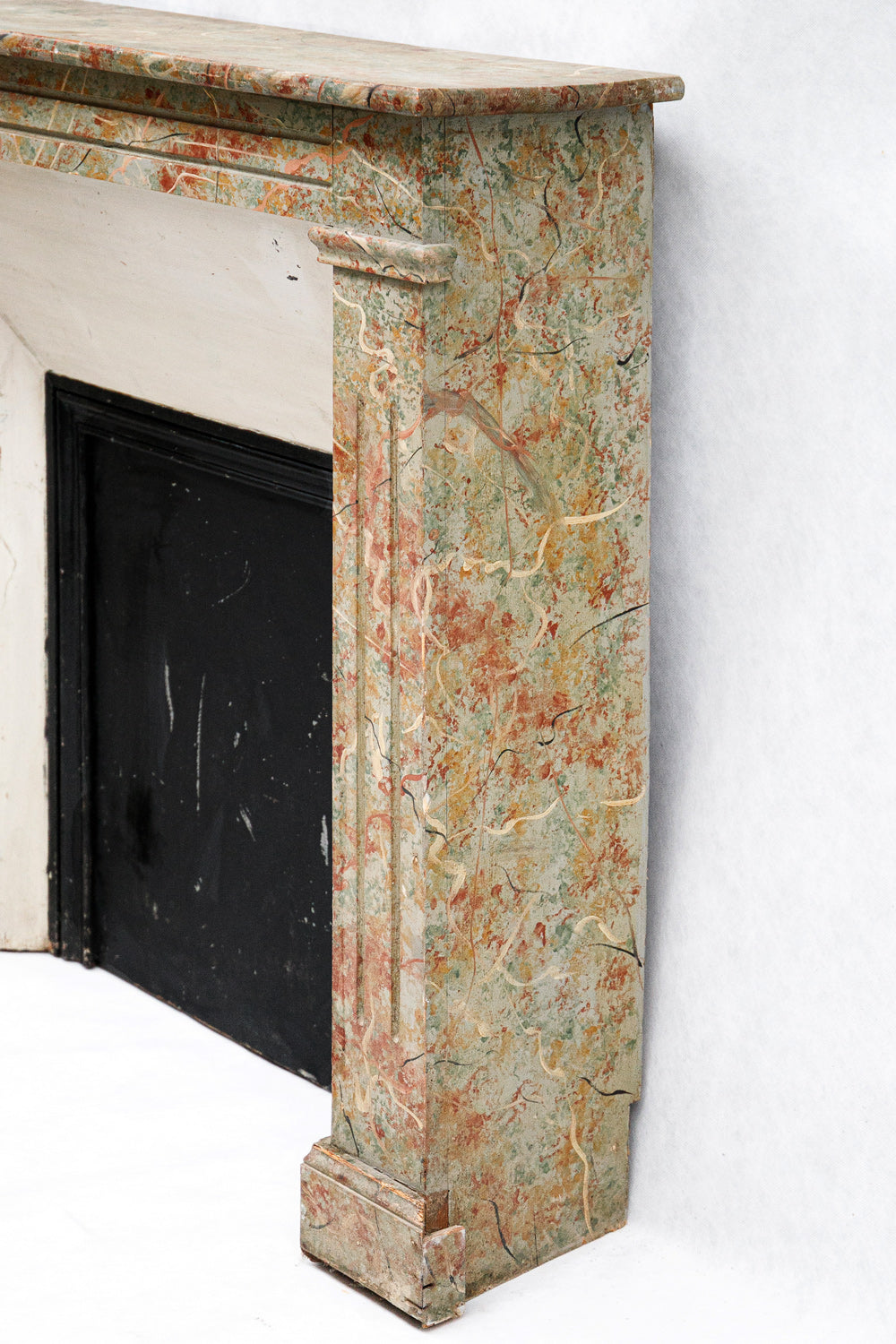 Sideview of an 19th century antique French fake painted marble fireplace with a colorful pattern on a white background