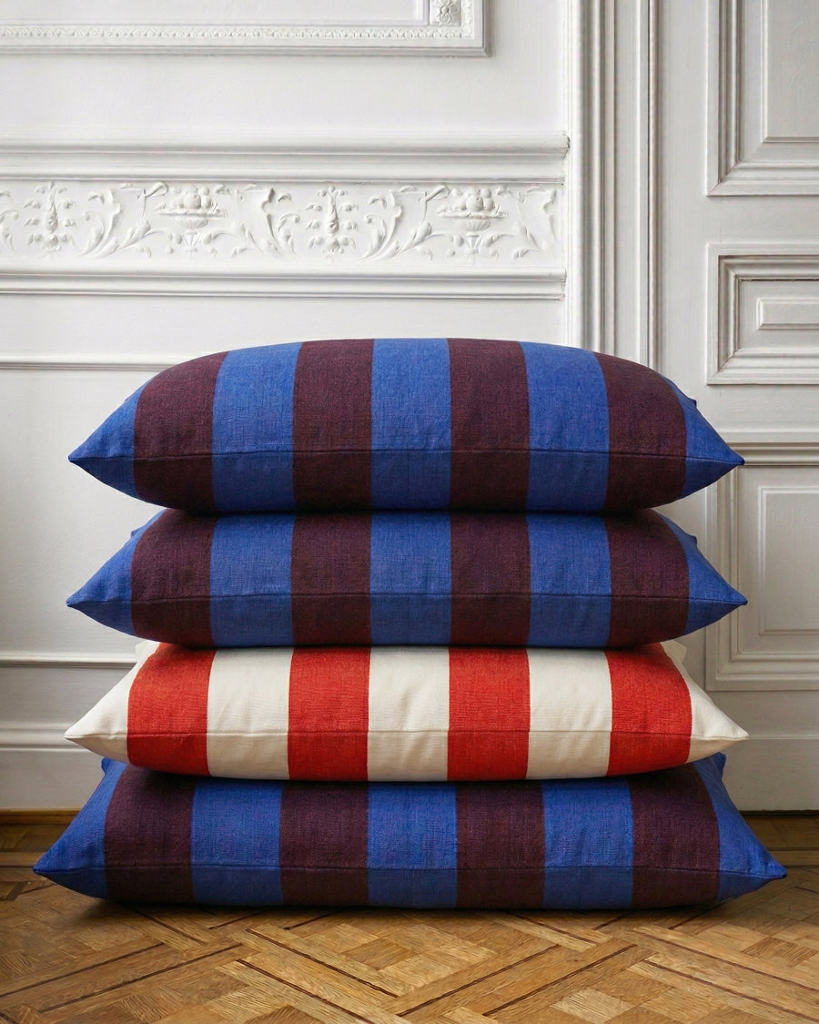 Stack of striped pillows in blue, red, and white on a wooden floor with decorative wall molding.