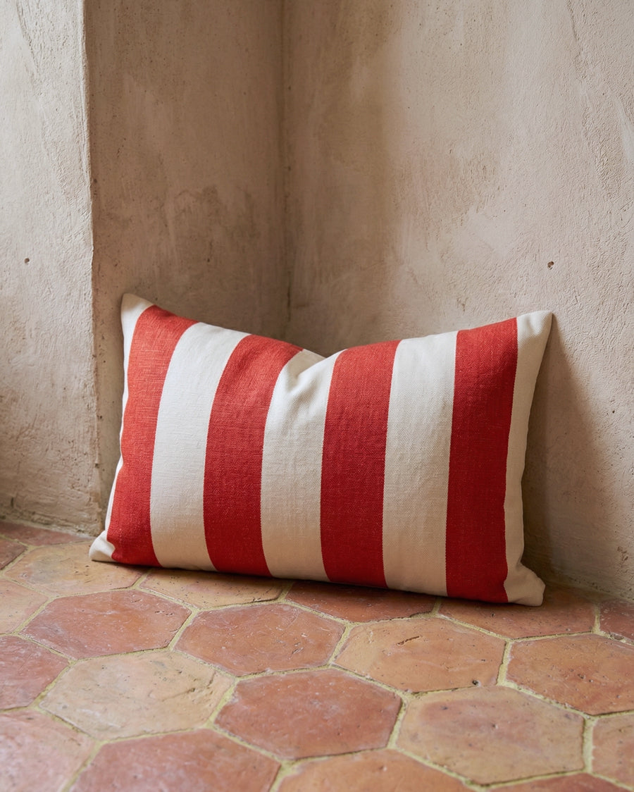 Red and white striped pillow on a terracotta floor against a beige wall, available via Wildschut Antiques.