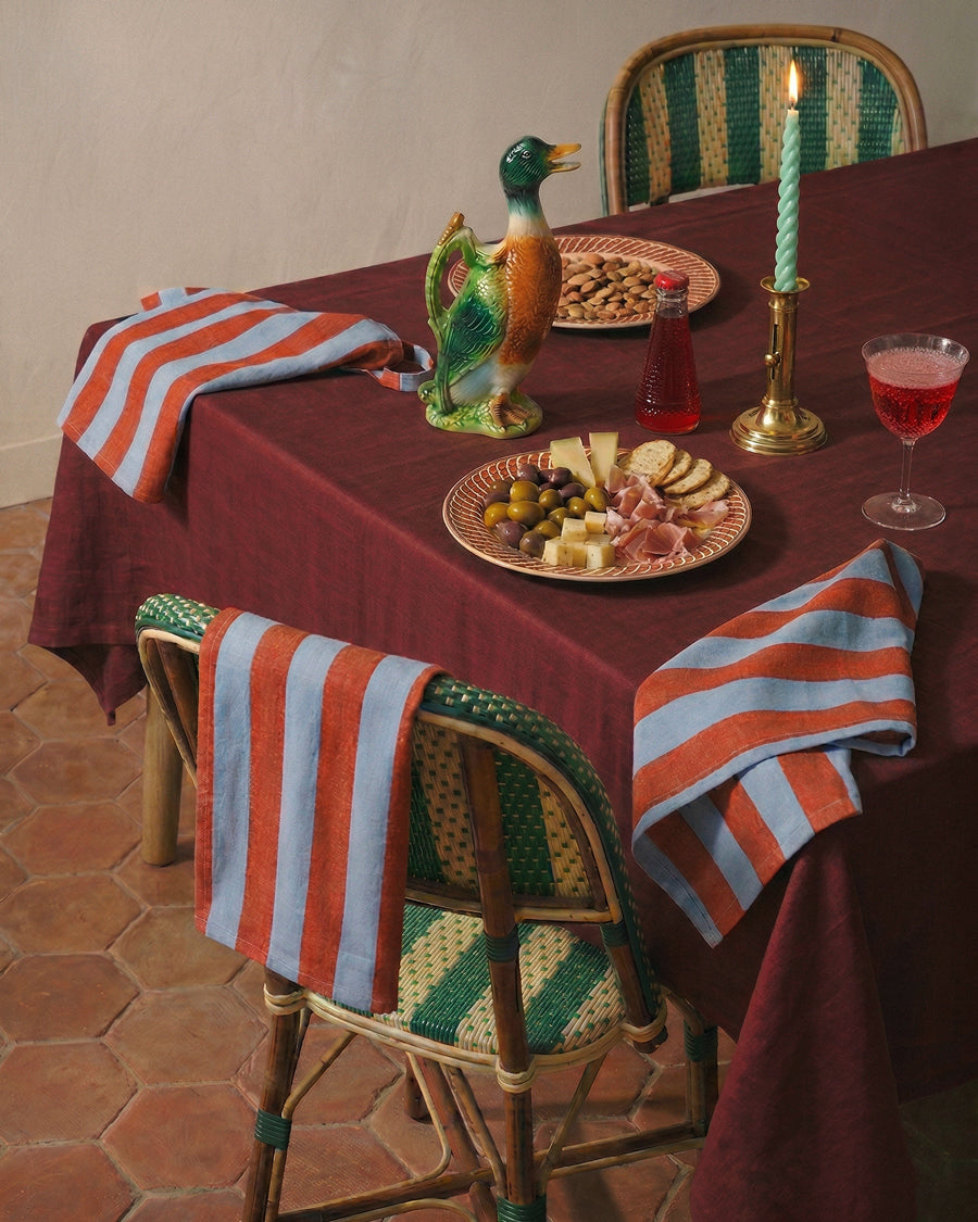 Dining table set with a plate of food, decanter, and candle on a striped tablecloth. Decorative items available via Wildschut Antiques.