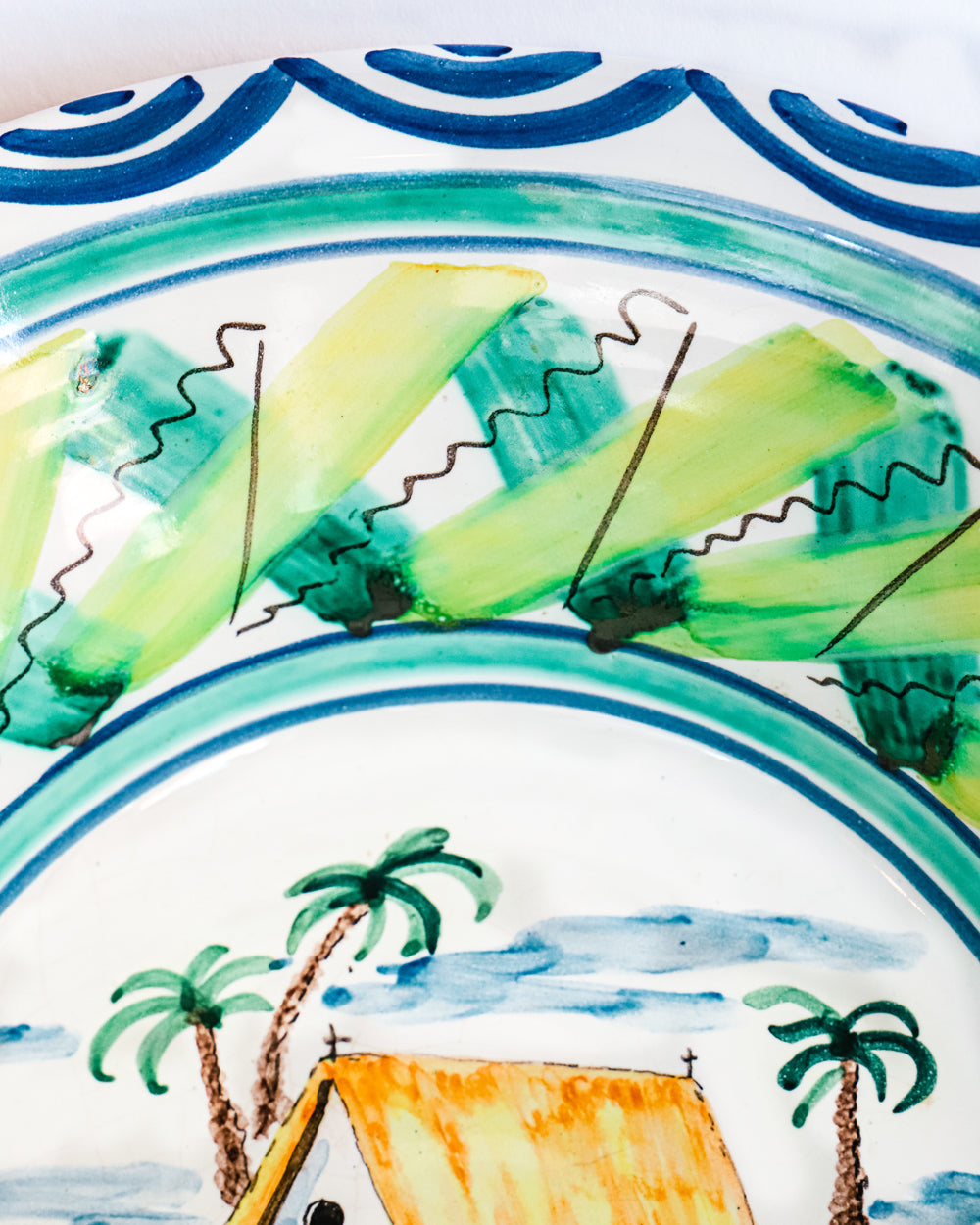Close-up of a vintage hand-painted Italian ceramic bowl with a house and palm trees design, predominantly blue and green in color