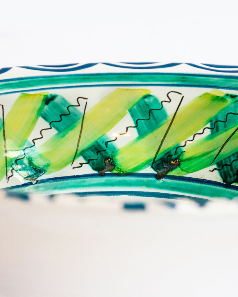 Close-up of a vintage hand-painted Italian ceramic bowl with a house and palm trees design, predominantly blue and green in color