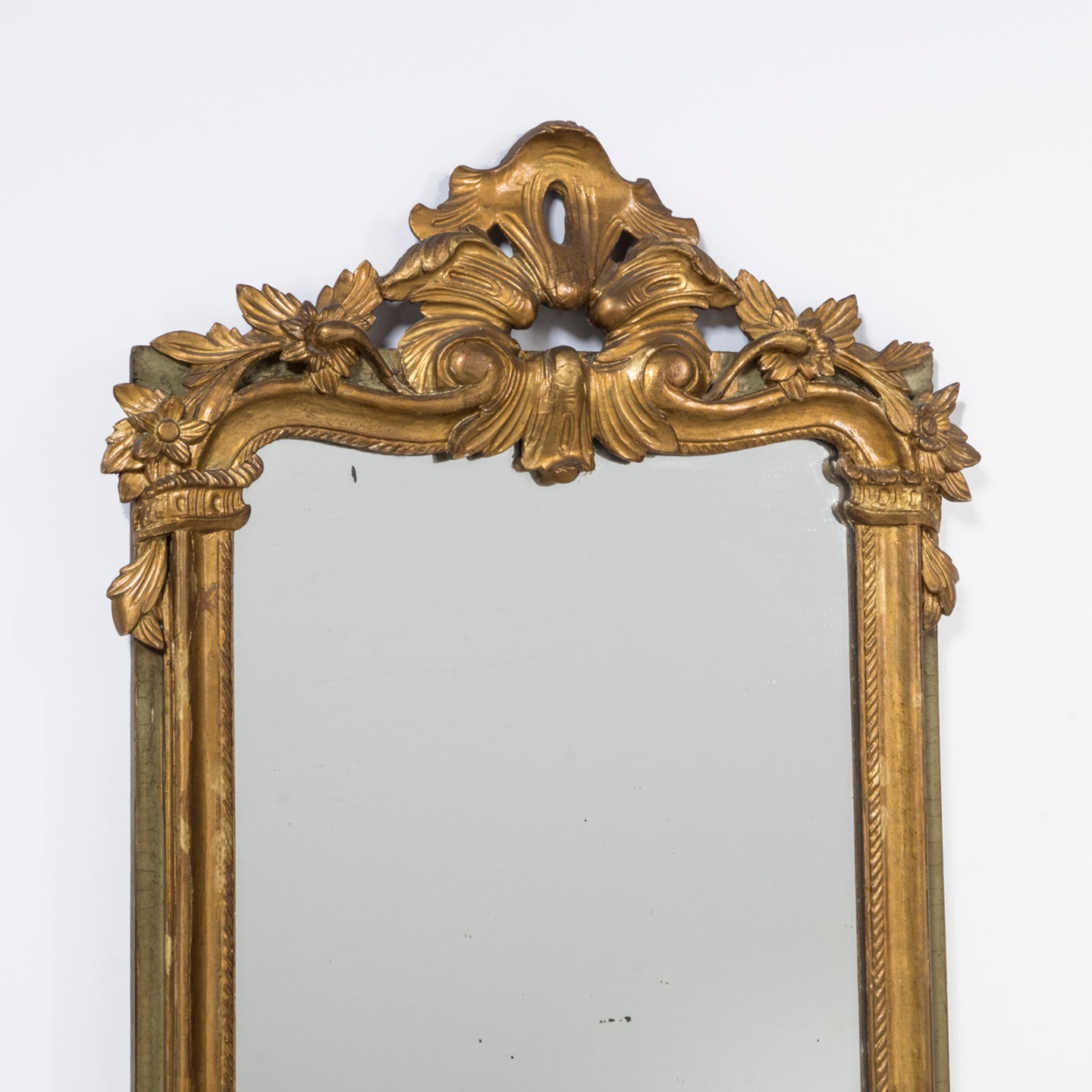 Close-up of the top part of a 19th C Antique Flower Mirror with rich carvings and a delicately crafted crown featuring leaves and flower motifs, with a soft green frame and authentic glass