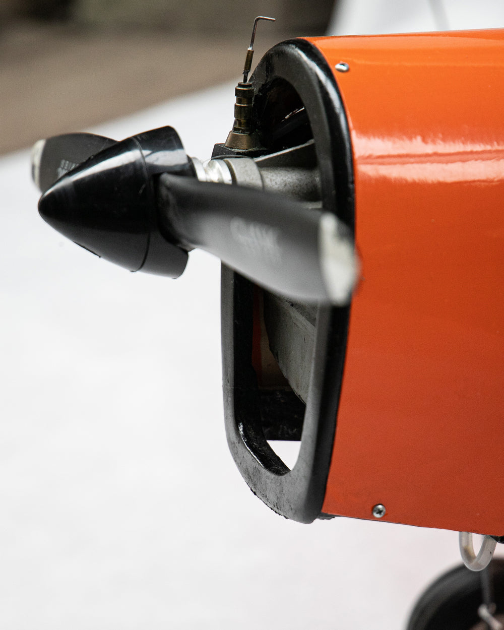Close-up of an orange and black aircraft engine housing with a black propeller blade attached, photographed against a light neutral background.
