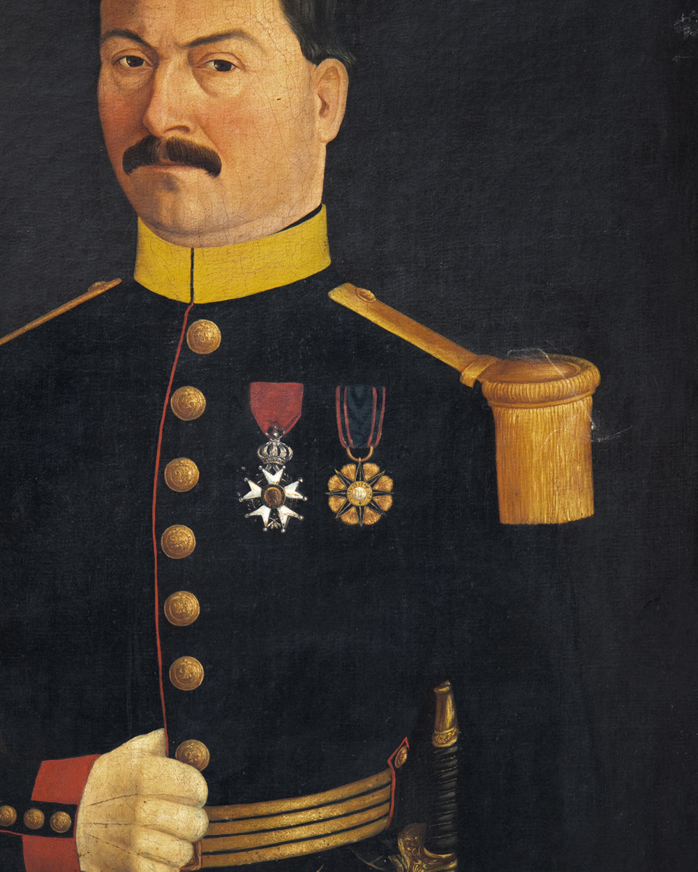 A painted portrait of a man in a dark military uniform with gold buttons, a yellow collar and medals on the chest, against a dark background. Close-up of an antique portrait of a French Military Man, ca, 1850 - 1870, available via Wildschut Antiques.