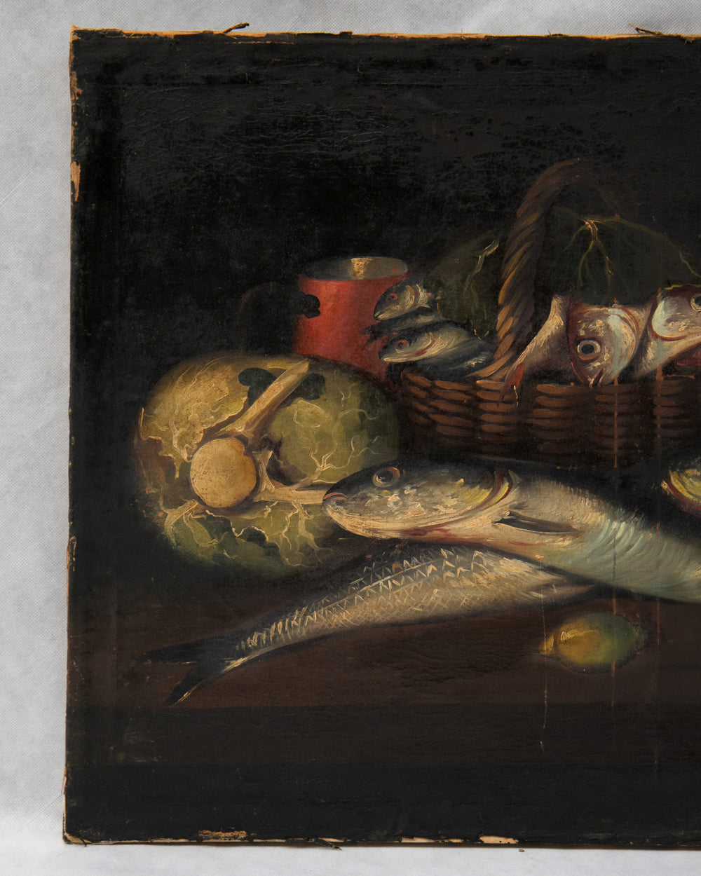 A still life painting detail showing fish, a cabbage, a red mug, and a basket of fish on a dark background. Detail of a Pair of Neapolitan Fish Still Lifes, 19th Century, available via Wildschut Antiques.