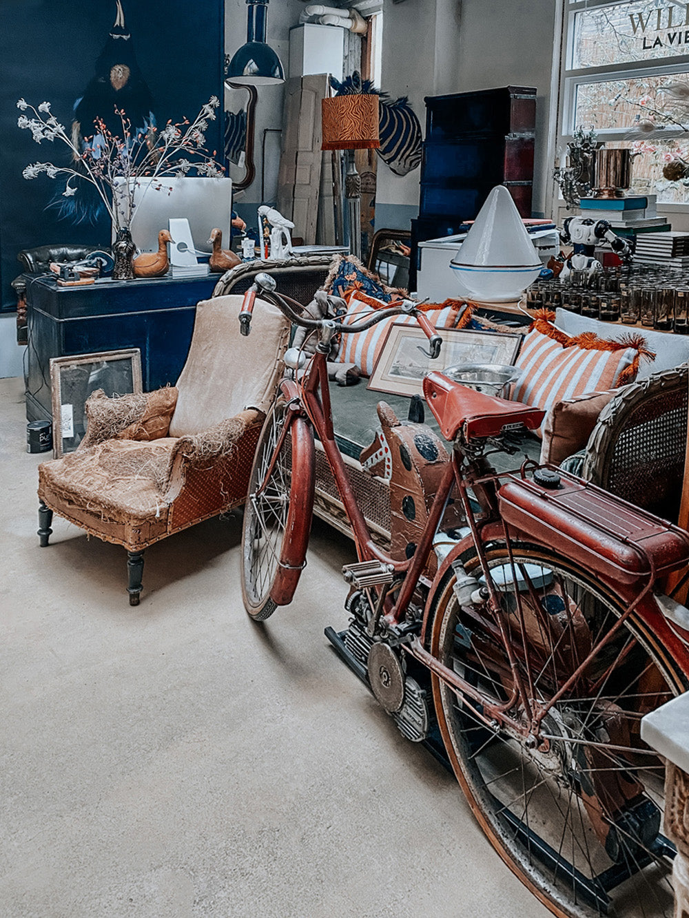 Wildschut Antiques warehouse showcasing an antique sofa and chair alongside a dark red French Mobylette motorcycle.