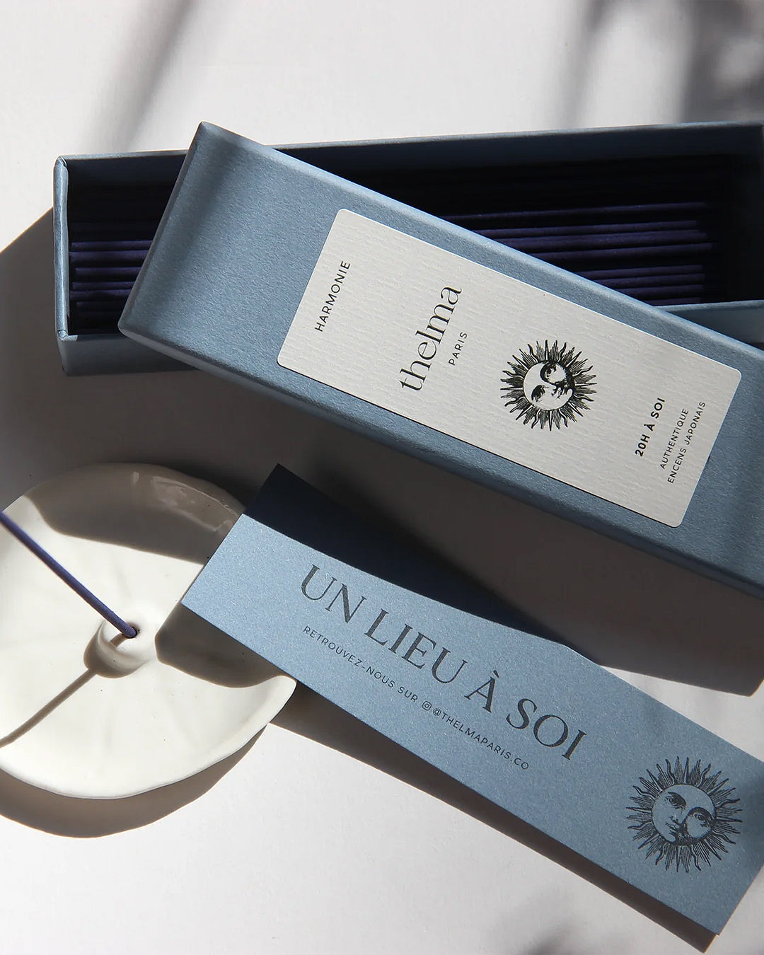 A package of Thelma Paris incense with several sticks visible outside the box, placed on a white surface with a candle next to it, available at Wildschut Antiques