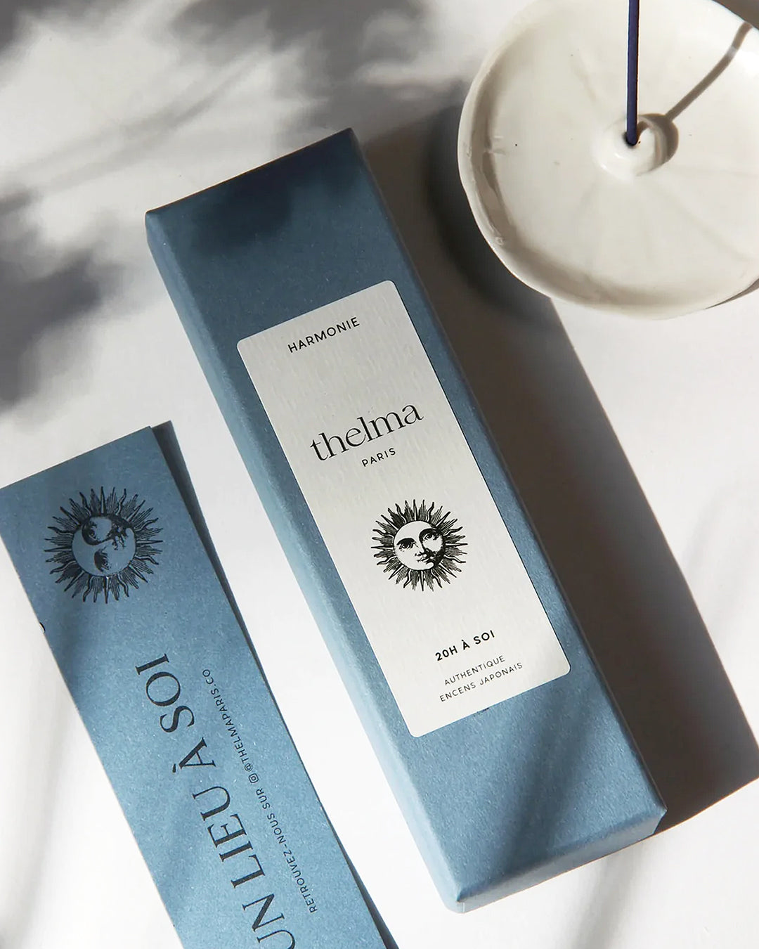 A box of Thelma Paris *Harmonie* incense displayed on a white surface, accompanied by a blue incense stick in a visible burner.