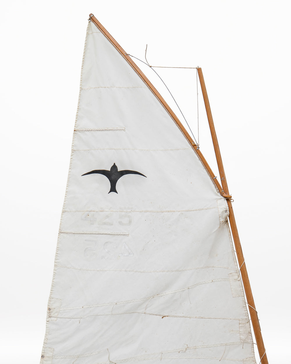 A white canvas sail on a wooden mast with a black bird - Valk - emblem printed on it, isolated against a solid white background.