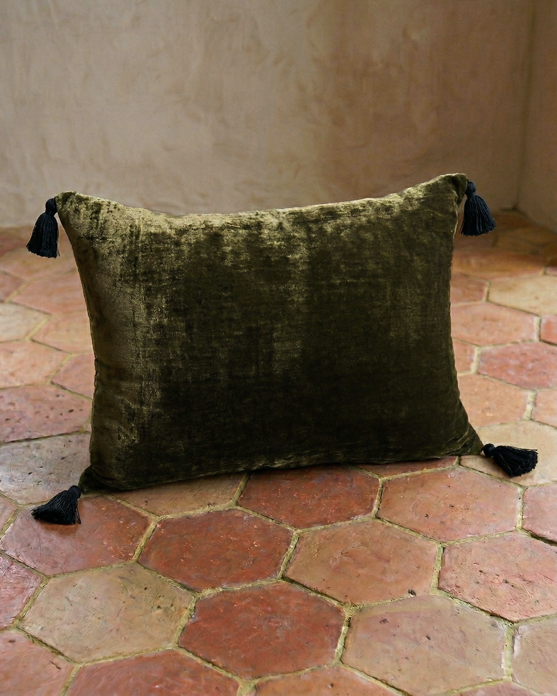 Green velvet pillow with tassels on a terracotta floor.