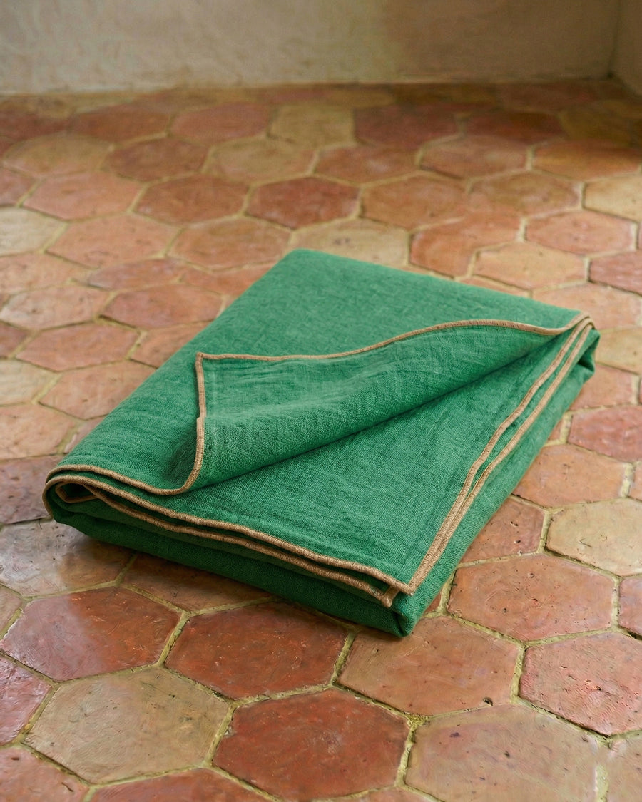 Folded apple green linen throw with beige brown trim on a terracotta tiled floor, available via Wildschut Antiques.