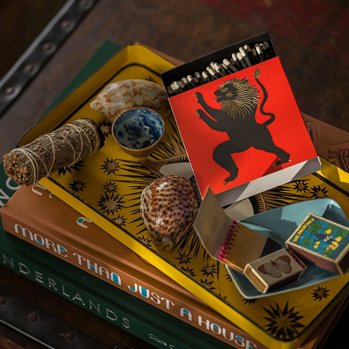 Matchbox with lion design on a stack of books and decorative items.