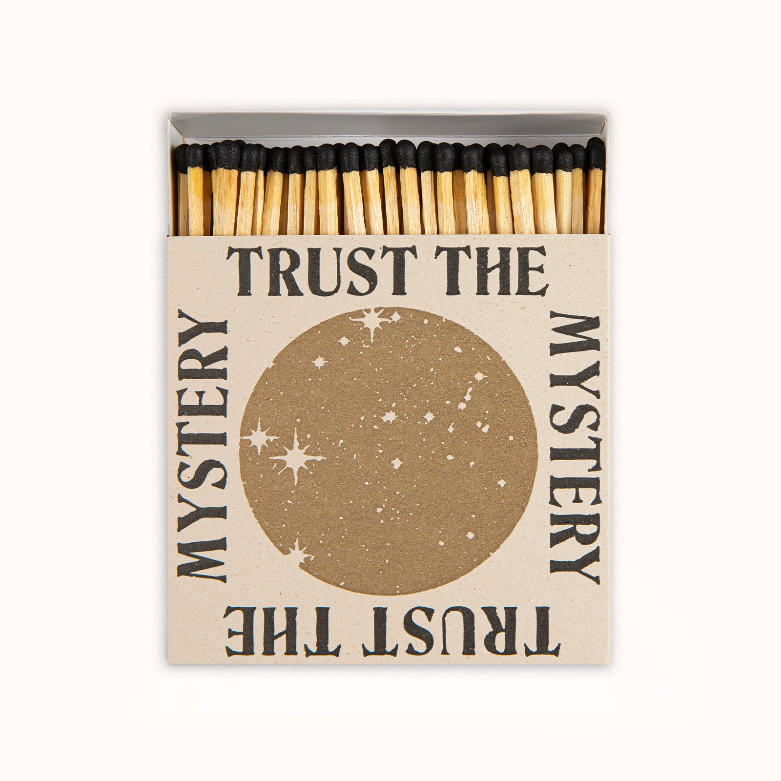 Matches in a decorative Archivist Gallery matchbox featuring a golden moon and the text 'Trust the Mystery', set against a black background, available at Wildschut Antiques.