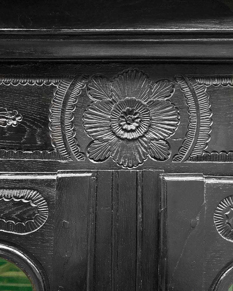 Close-up of a dark wooden panel with floral carvings belonging to an antique French Marriage armoire.