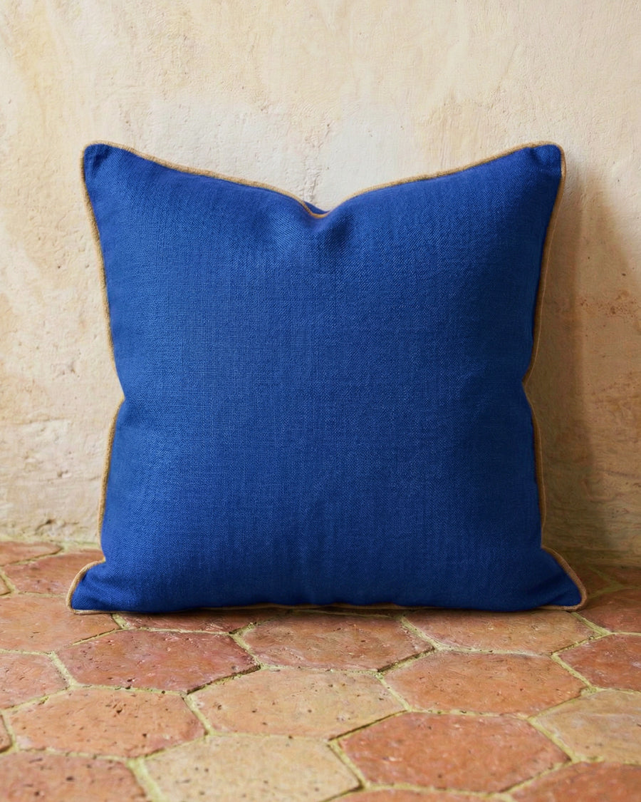 Blue linen pillow on a terracotta stone floor with a beige wall background, available via Wildschut Antiques.