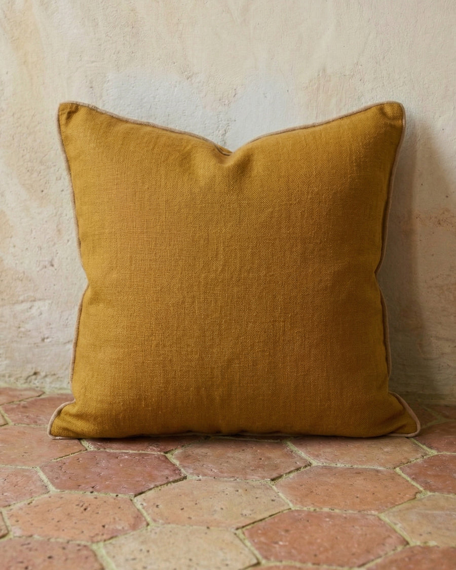 Ginger brown linen pillow on a textured terracotta stone floor, available via Wildschut Antiques.