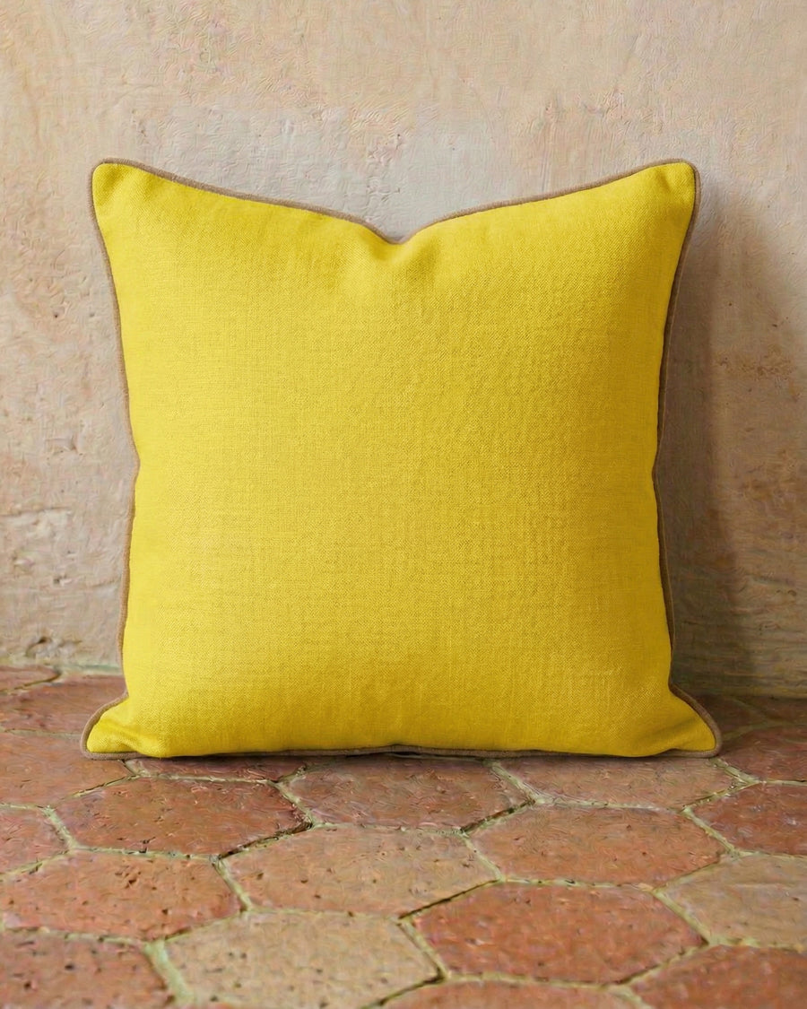 Yellow linen pillow on a textured terracotta stone floor, available via Wildschut Antiques.