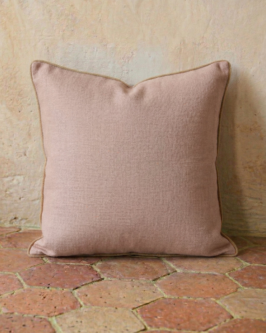 Soft pink linen pillow on a textured terracotta stone floor, available via Wildschut Antiques.