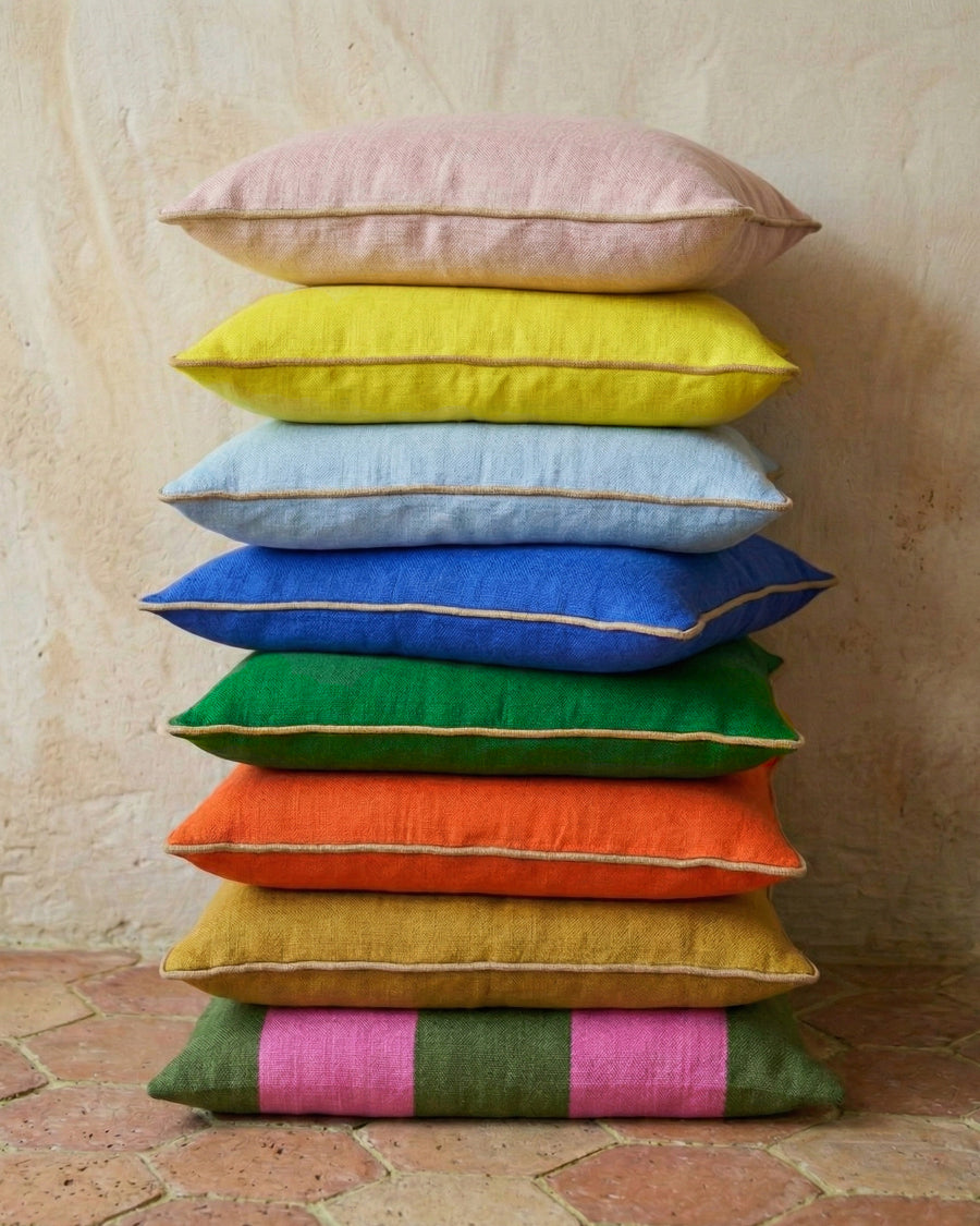 Stack of colorful pillows on a textured terracotta tiled floor, available via Wildschut Antiques.