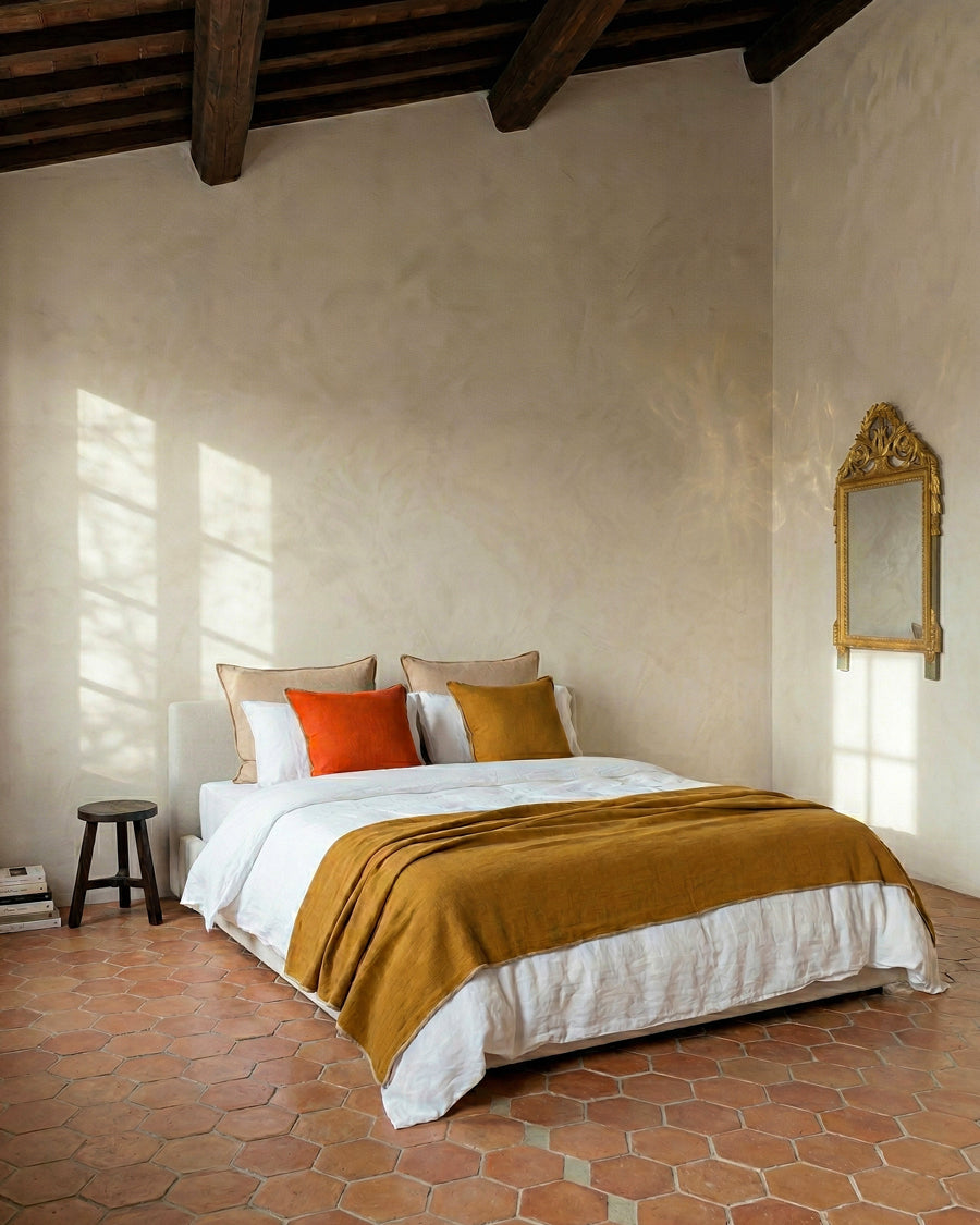 Bedroom with terracotta floor, beige walls, and a wooden ceiling, an antique marriage mirror hanging on the wall, available via Wildschut Antiques.
