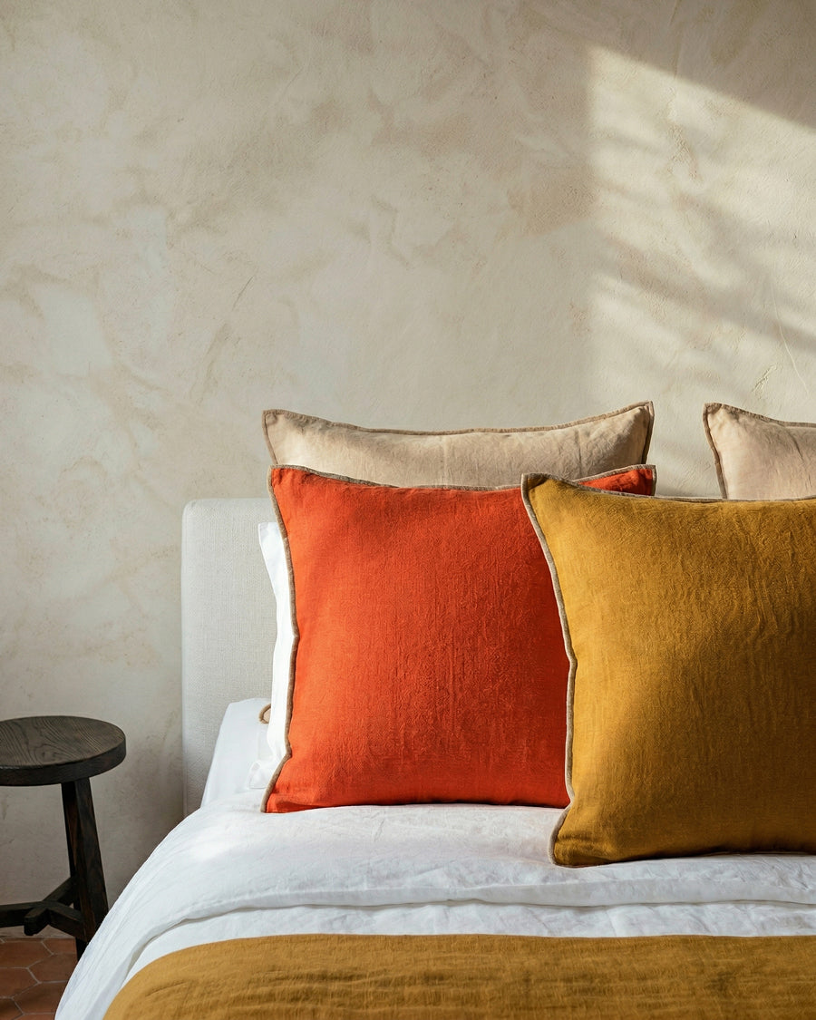 Bed with orange and ginger brown pillows against a beige wall. 