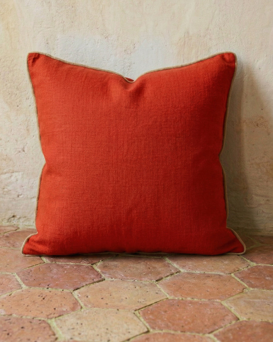 Tomato red linen pillow on a textured terracotta stone floor, available via Wildschut Antiques.